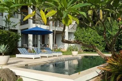 a pool with chairs and an umbrella next to a building at Casa Ohana - 5 BR Ocean Front Home in Playa Negra, CRC in Playa Negra
