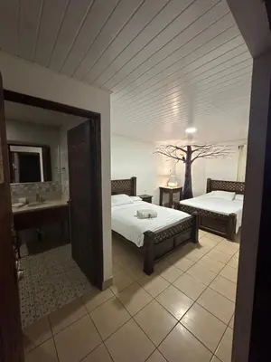 a bedroom with two beds and a bathroom with a sink at Hotel Pacande B&B in Alajuela City