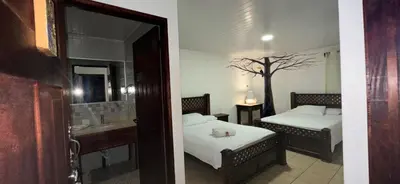 a bedroom with two beds and a bathroom with a tree at Hotel Pacande B&B in Alajuela City