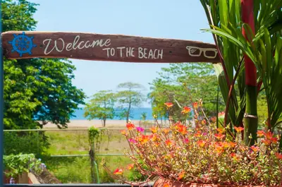 a wooden welcome to the beach sign in a garden at La Hacienda Rooms & Food in Jacó