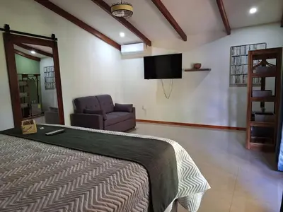 a bedroom with a bed and a chair and a television at Olla é Mono Ecolodge in Sarapiquí