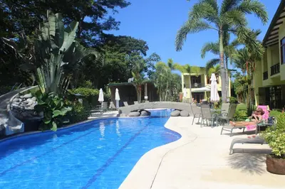 a pool at a resort with chairs and palm trees at Club Del Cielo Unit 1 in Jacó