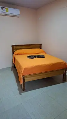 a bed in a room with an orange comforter at Hospedaje Arboleda in Quepos