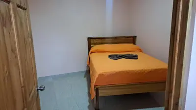 a small bedroom with a bed with an orange blanket at Hospedaje Arboleda in Quepos
