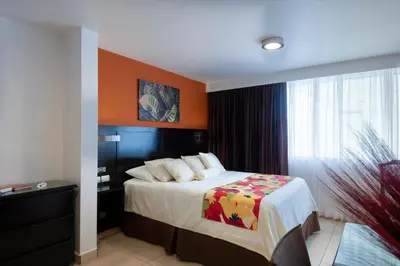 a bedroom with a bed with an orange wall at Hotel Residence Inn Suites Cristina in San José