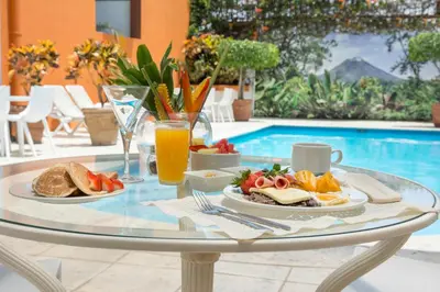a glass table with breakfast food and drinks next to a pool at Hotel Residence Inn Suites Cristina in San José