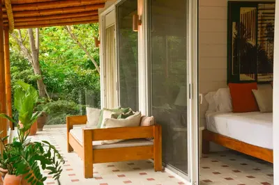 a porch with a chair and a bed and a window at Tree NestNido 2- Ocean view- 5 min walk to beac in Santa Teresa Beach