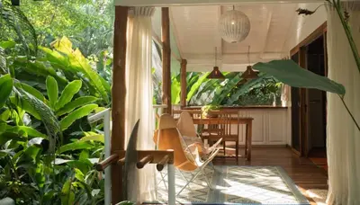 a porch with a chair and a table and some plants at Surf Casitas - Mid Tide Bungalow in Santa Teresa Beach