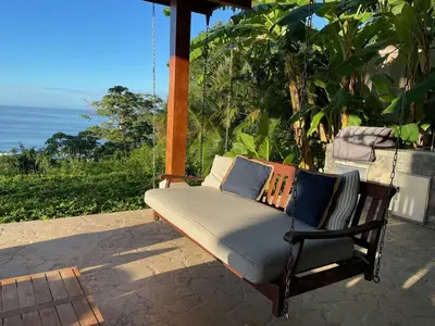 a bench on a porch with the ocean in the background at Casa Colibri - Stunning ocean view in Santa Teresa Beach