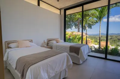 two beds in a bedroom with large windows at Mahalo Villas in Playa hermosa