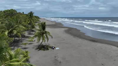 a person sitting on a beach with a surfboard at 2 Bedroom Oceanfront Condo with Wi-Fi, AC and Pool in Bejuco