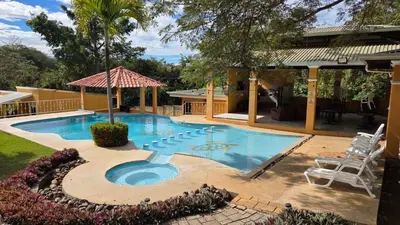 a swimming pool in a yard with two chairs and a house at Villa Jr 3, Piscina y Naturaleza, SJO Airport 80min in Tarcoles