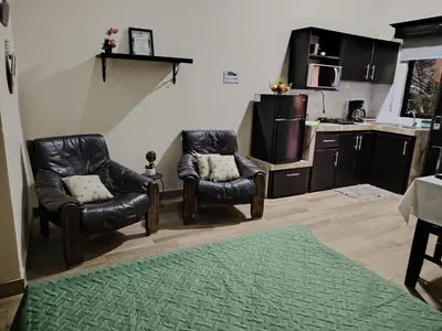 a living room with two leather chairs and a kitchen at Villa Jr 3, Piscina y Naturaleza, SJO Airport 80min in Tarcoles