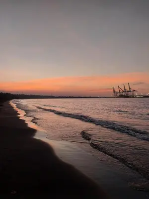 a sunset on the beach with windmills in the background at Apartamento de playa del Caribe in Moín
