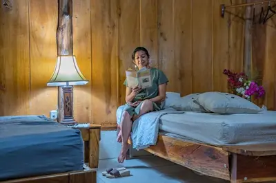 a woman sitting on a bed reading a book at Helenors estancia in Nicoya