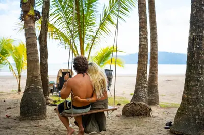 a man and woman sitting on a swing on the beach at 8-min Walk to Beach with Pool & Golf in Pochote