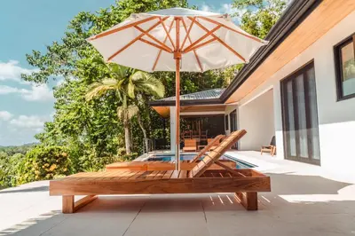 a patio with an umbrella and chairs and a pool at Arbórea Villas in Chontales