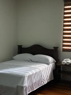a bedroom with a bed with white sheets and a window at Chato Arenal Lodge in Fortuna