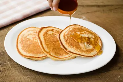 a person is pouring syrup onto two pancakes on a plate at Hotel Boyeros in Liberia