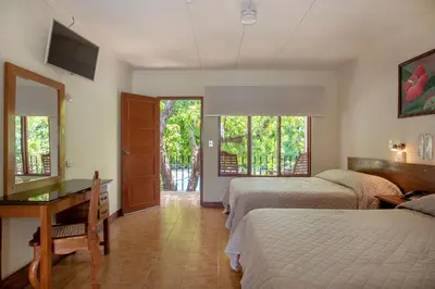 a bedroom with two beds and a desk and a window at Hotel Boyeros in Liberia