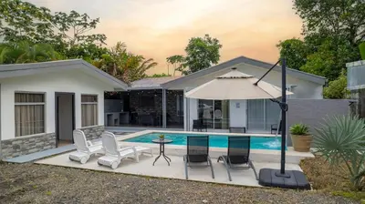 a pool with chairs and an umbrella next to a house at Villa Diriá La Fortuna - Downtown Home in Fortuna