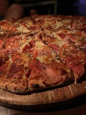 a pizza with tomatoes and cheese on a wooden cutting board at Casa Club Bluaska in Sarapiquí