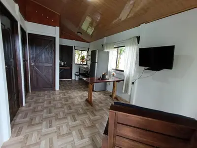 a living room with a table and a television and a kitchen at Ibis House, Bijagua in Upala