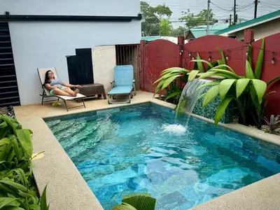 a woman sitting in a chair next to a swimming pool with a waterfall at Villa Jade La Fortuna, Family in Fortuna