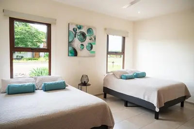 two beds in a room with two windows at La Perla Cozy 3BR sleeps 10 Hacienda Pinilla in Santa Cruz