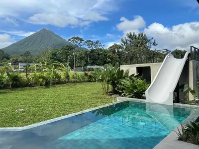 a pool with a slide in a yard with a mountain at Xanadu Arenal Villa in Fortuna