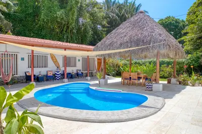 a swimming pool with a thatched umbrella and tables and chairs at Mariposa Monarca in Esterillos