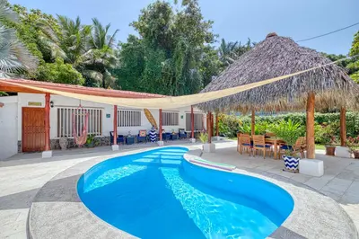a pool with a thatched umbrella and chairs and tables at Mariposa Monarca in Esterillos