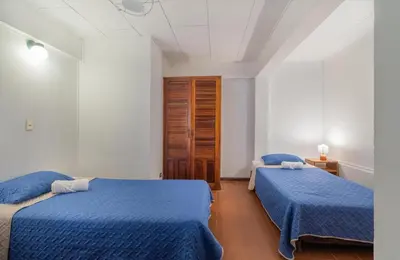 two beds in a white room with blue sheets at Hotel el Tajalin in Montezuma