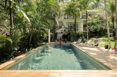 a woman standing next to a swimming pool in front of a house at Sukha at Namaste Oasis Condo in Nosara