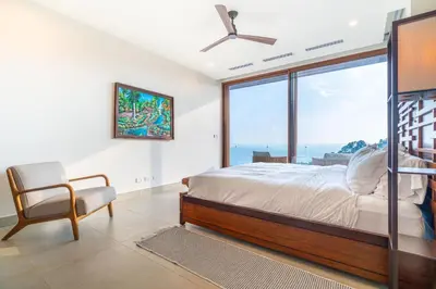 a bedroom with a bed and a chair and a large window at Casa Bella Vina - by Pura Villas in Dominical