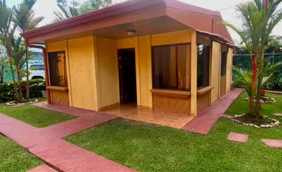 a small yellow house with a grass yard at Villas BRENES in Uvita