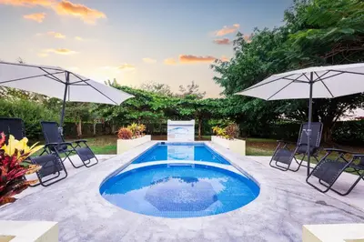 a swimming pool with two umbrellas and chairs at Villa Tropical by Vacation Pura Vida in Esterillos Este