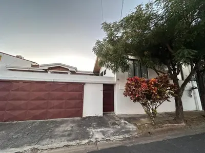 a house with a red garage door and a tree at Hotel Boutique CasAguacate close to Airport, Pedregal, Centro de Convenciones de Costa Rica in Potrerillos