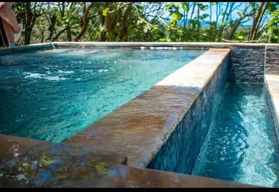 a swimming pool with blue water and a stone wall at Fruta mango # 3 in Playa Guacalillo