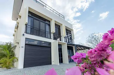 a white house with a black garage door at Casa Buena Vista with Incredible Ocean Views in Playa Hermosa