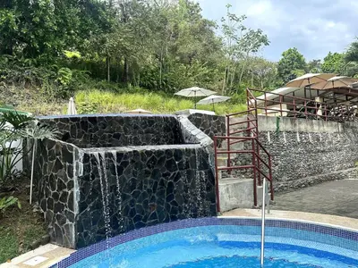 a swimming pool with a stone wall and a waterfall at Herradura casa vacacional in Herradura
