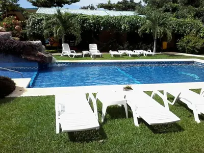 a pool with white tables and chairs next to it at Apartments-Villas Playa Potrero 1 in Potrero