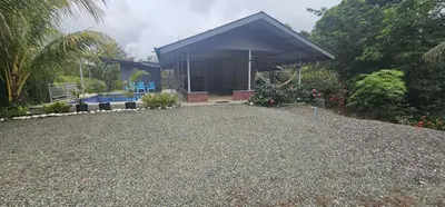 a house with a blue roof on a gravel driveway at Cabaña y Piscina el Lorito in Uvita