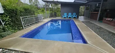 a swimming pool with two blue chairs and a house at Cabaña y Piscina el Lorito in Uvita