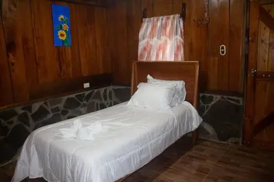 a bedroom with a bed with white sheets and pillows at Higuitos Lodge Cabaña in San Luis