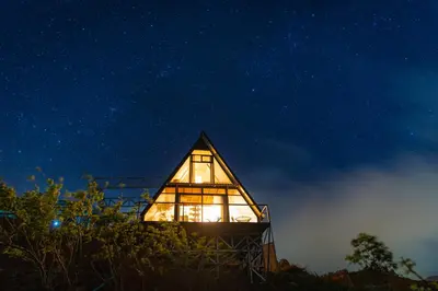 a glass house with a lit up window at night at A Frame Home in Cebadilla