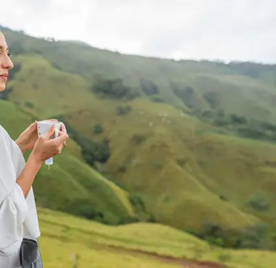 a woman holding a cup in front of a mountain at A Frame Home in Cebadilla