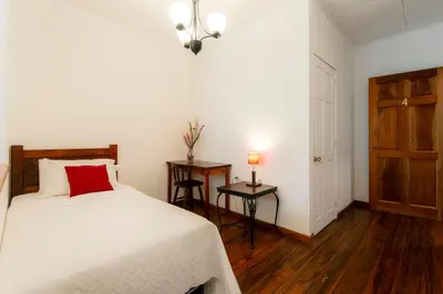 a bedroom with a bed and a table with a red pillow at Habitación triple confort - Casa Esmeralda in San José