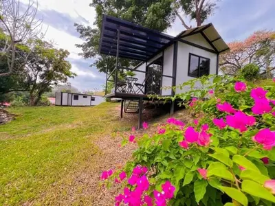 a small house with a bench and pink flowers at Jalapa's Rural Container Studio in Tilarán
