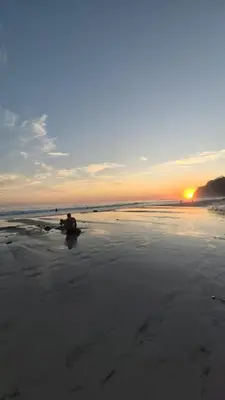 a person sitting on a surfboard on the beach at sunset at Bus hotel Playa Barrigona, entre Sàmara y Nosara in Nicoya